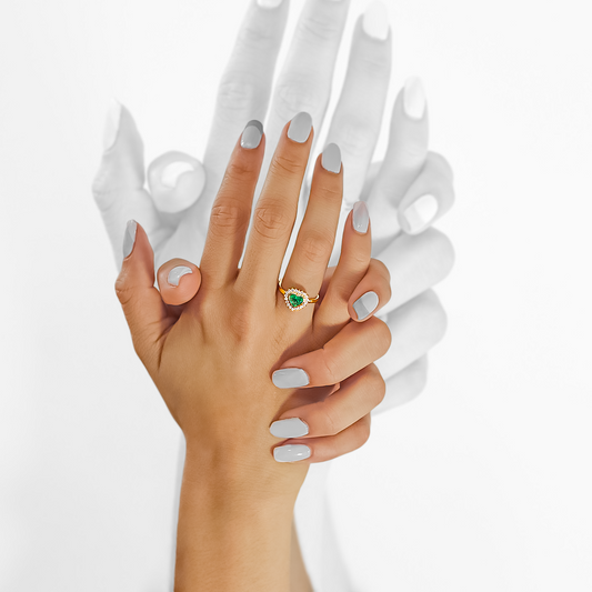 Mano de mujer usando anillo con forma de corazón en el centro en oro amarillo de 18 quilates, piedra esmeralda de color verde en forma de corazón y 20 diamantes de color blanco alrededor, hecho en Joyería Caracas. 