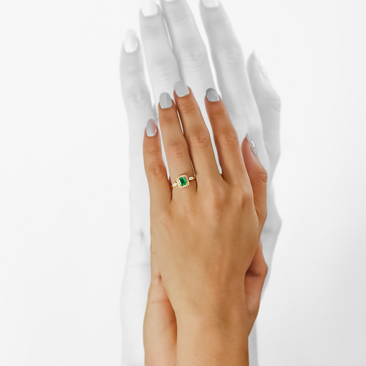 Mano de mujer con anillo en oro amarillo de 18 quilates, piedra esmeralda en el centro, 2 diamantes en corte marquise de color blanco y 16 diamantes de color blanco alrededor, hecho en Joyería Caracas. 