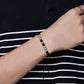 Mano de hombre usando una pulsera tejida en hilo de color negro con accesorios del mismo color y esferas facetadas en oro amarillo y blanco de 18 quilates de Joyería Caracas. 