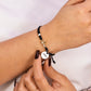 Mano de mujer con pulsera tejida en hilo negro coreano y accesorios de bisutería en color negro y blanco y dije en forma de niña y perrito en oro amarillo de 18 quilates con cristales de color blanco, hecho en Joyería Caracas. 