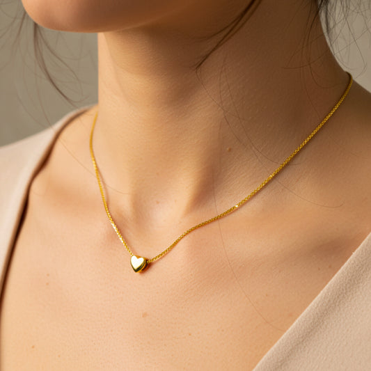 Cuello de mujer usando una gargantilla con cadena en tejido Bismarck con dije pasante en forma de corazón en oro amarillo de 18 quilates de Joyería Caracas. 
