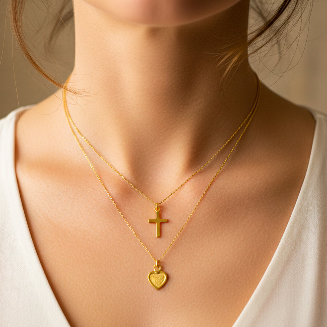 Cuello de mujer usando una gargantilla con dije en forma de cruz y corazón en oro amarillo de 18 quilates de Joyería Caracas. 
