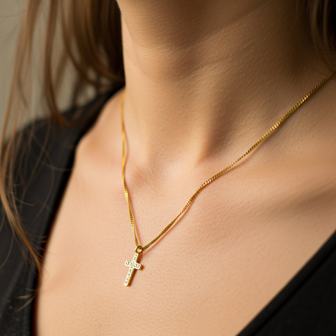 Cuello de mujer usando una gargantilla con tejido mini cubano con dije en forma de cruz en oro amarillo de 18 quilates con cristales de color blanco de Joyería Caracas. 