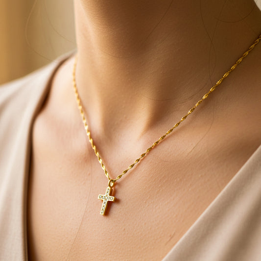 Cuello de mujer usando una gargantilla con cadena en tejido Singapur con dije de cruz en oro amarillo de 18 quilates con cristales de color blanco de Joyería Caracas. 