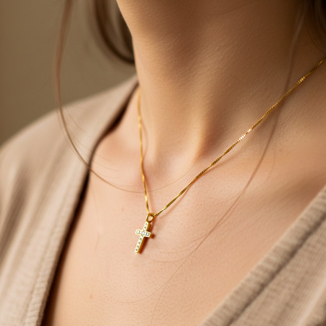 Cuello de mujer usando una gargantilla con cadena en tejido Venecia con dije en forma de cruz en oro amarillo de 18 quilates de Joyería Caracas. 