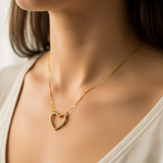 Cuello de mujer usando una gargantilla con cadena en tejido Venecia y dije de corazón en oro amarillo de 18 quilates con cristal de color blanco de Joyería Caracas. 