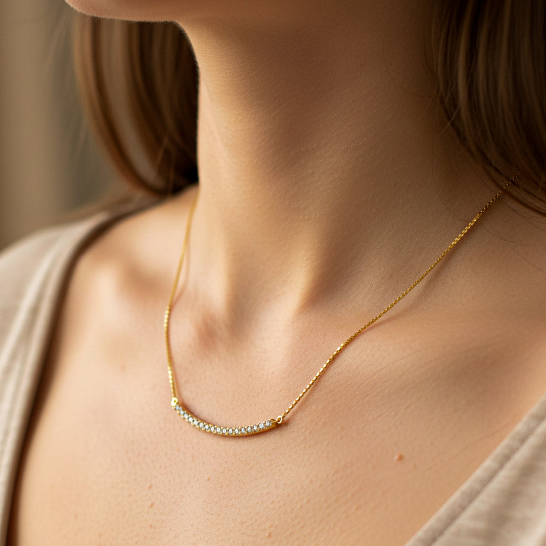 Cuello de mujer usando una gargantilla con una barra ondulada en oro amarillo de 18 quilates con cristales de color blanco de Joyería Caracas. 