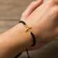 Mano de mujer usando una pulsera tejida con hilo de color negro y herraje en forma de avión en oro amarillo de 18 quilates de Joyería Caracas. 