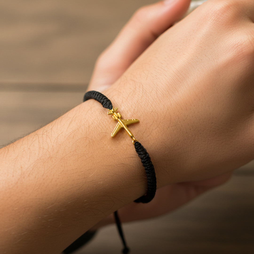 Mano de mujer usando una pulsera tejida con hilo de color negro y herraje en forma de avión en oro amarillo de 18 quilates de Joyería Caracas. 