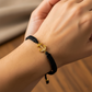 Mano de mujer usando una pulsera tejida en hilo de color negro con herraje en forma de ancla en oro amarillo de 18 quilates con cristales de color blanco de Joyería Caracas. 