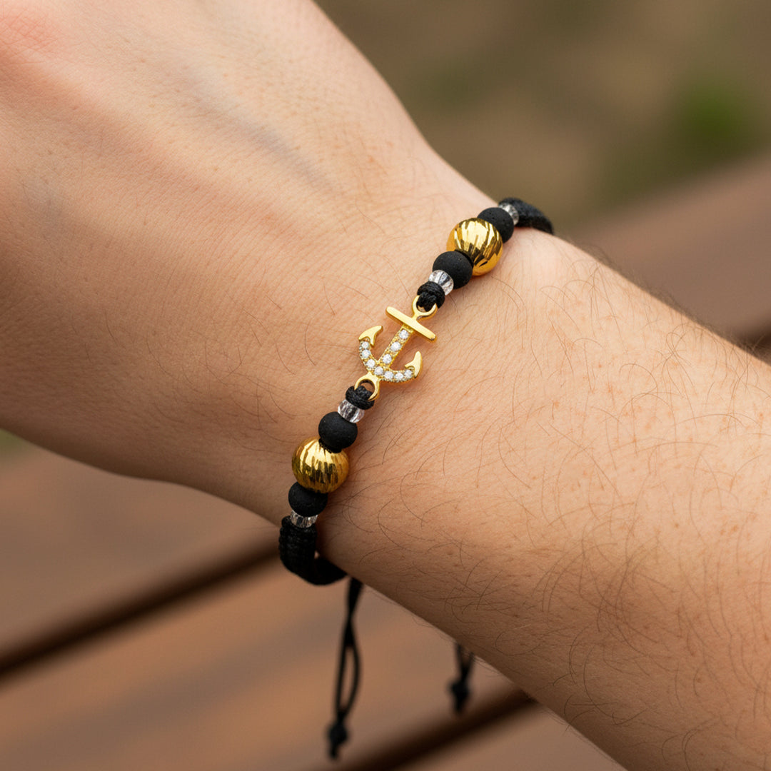 Mano de modelo usando una pulsera tejida con ancla y esferas facetadas en oro amarillo de 18 quilates con bisutería de calidad de Joyería Caracas. 