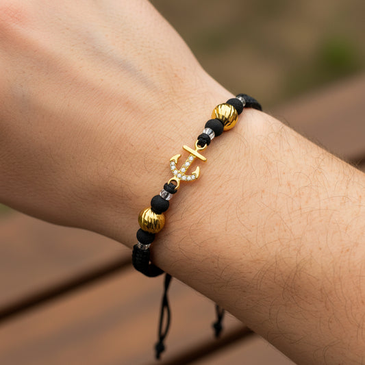 Mano de modelo usando una pulsera tejida con ancla y esferas facetadas en oro amarillo de 18 quilates con bisutería de calidad de Joyería Caracas. 