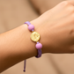 Mano de modelo usando una pulsera tejida en hilo color lila con herraje de Árcangel San Rafael de Joyería Caracas. 