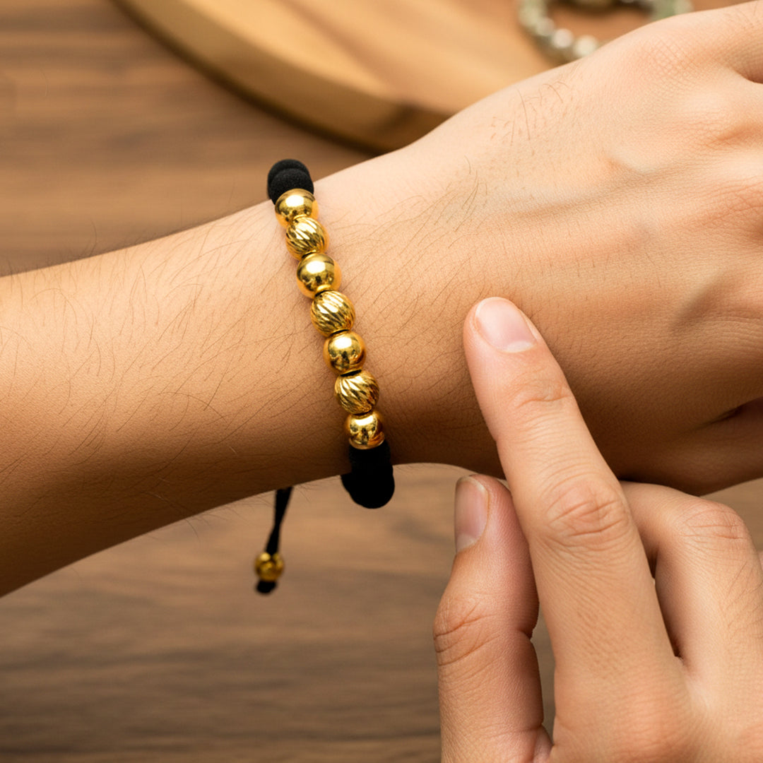 Mano de modelo usando una pulsera tejida en hilo de color negro con esferas lisas y facetadas en oro amarillo de 18 quilates con bisutería de calidad de Joyería Caracas. 