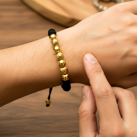 Mano de modelo usando una pulsera tejida en hilo de color negro con esferas lisas y facetadas en oro amarillo de 18 quilates con bisutería de calidad de Joyería Caracas. 