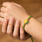 Mano de modelo usando una pulsera tejida en hilo color verde y amarillo con dije del Atlético Bucaramanga y esferas lisas en oro amarillo de 18 quilates de Joyería Caracas. 