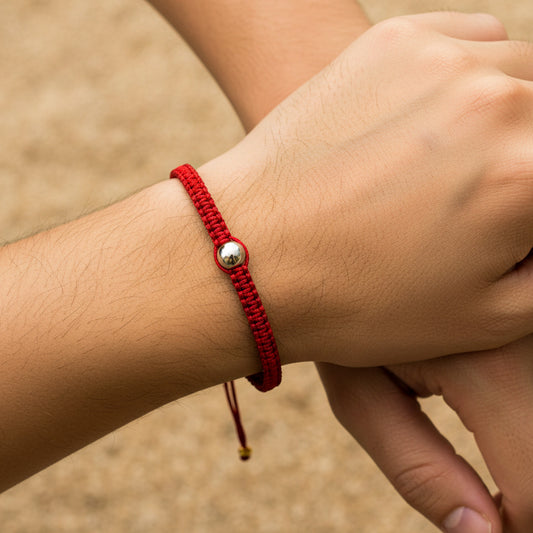 Mano de modelo usando una pulsera tejida en hilo de color rojo con esfera lisa en el centro en oro blanco de 18 quilates de Joyería Caracas. 