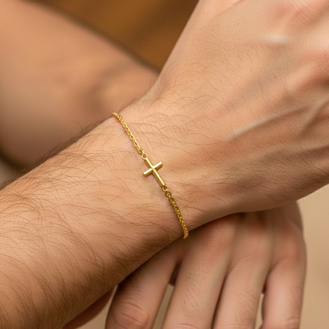 Mano de hombre usando una pulsera tejida en tejido Bismarck con cruz en oro amarillo de 18 quilates de Joyería Caracas. 
