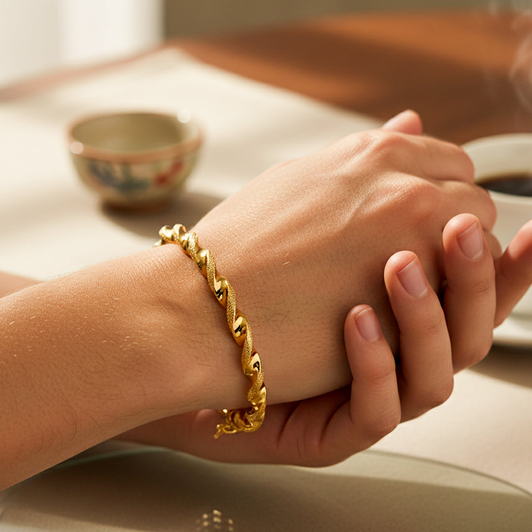 Mano de mujer usando una pulsera brazalete en forma de melcocha con textura de arena en oro amarillo de 18 quilates de Joyería Caracas. 