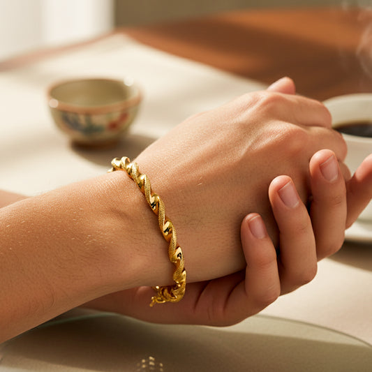 Mano de mujer usando una pulsera brazalete en forma de melcocha con textura de arena en oro amarillo de 18 quilates de Joyería Caracas. 