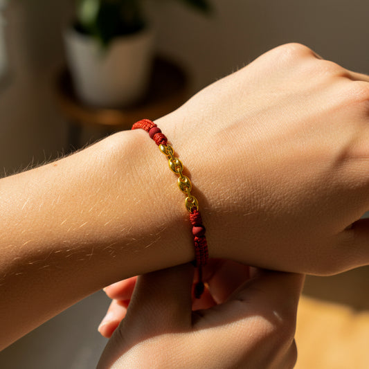 Mano de modelo usando una pulsera tejida en hilo rojo con tejido calabrote en oro amarillo de 18 quilates con bisutería de calidad de Joyería Caracas. 