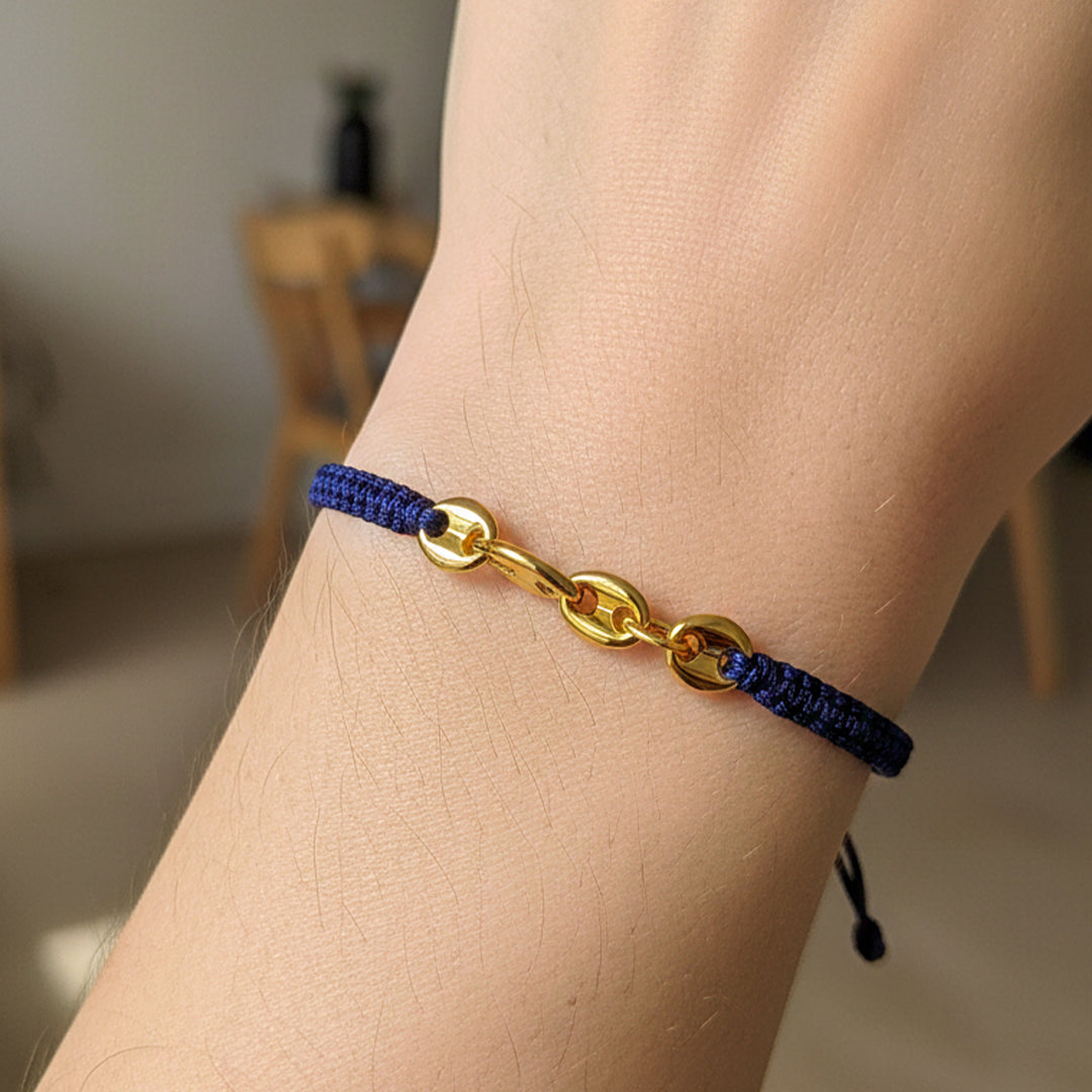 Mano de modelo usando una pulsera tejida en hilo color azul oscuro con herraje en tejido calabrote en oro amarillo de 18 quilates de Joyería Caracas. 