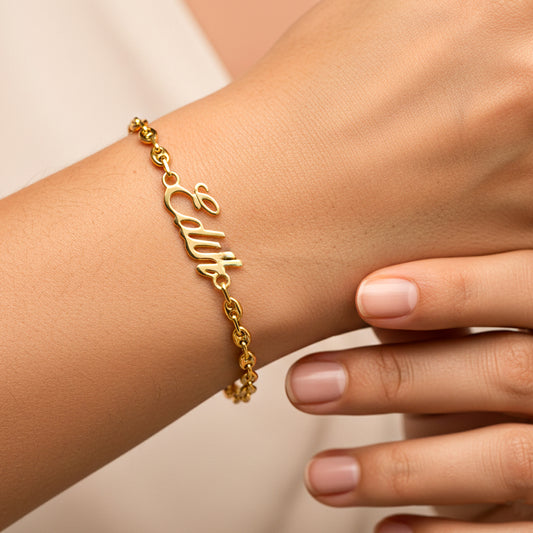 Mano de mujer usando una pulsera con tejido calabrote y nombre personalizado en oro amarillo de 18 quilates de Joyería Caracas. 