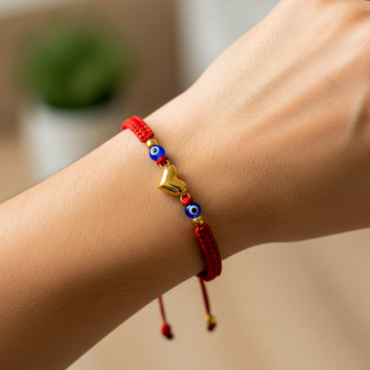 Mano de modelo usando una pulsera tejida de hilo color rojo, herraje en forma de corazón y 2 esferas lisas de color amarillo de 18 quilates con bisutería de calidad de Joyería Caracas. 