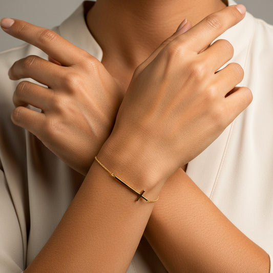 Mano de mujer usando una pulsera con herraje de cruz en oro amarillo de 18 quilates de Joyería Caracas. 