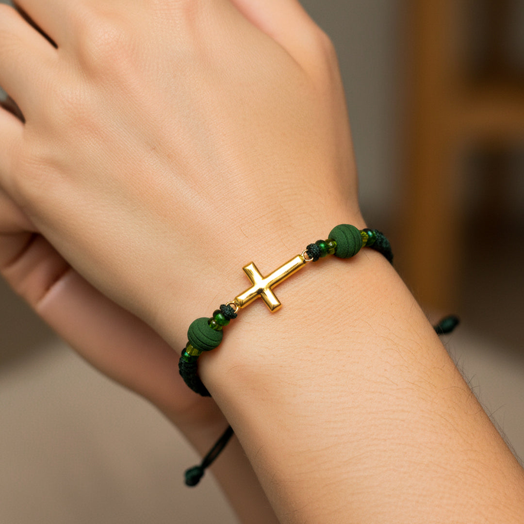 Mano de modelo usando una pulsera tejida en hilo color verde oscuro con dije de cruz en oro amarillo de 18 quilates con bisutería de calidad de Joyería Caracas. 