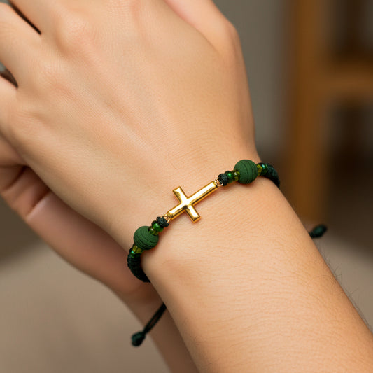 Mano de modelo usando una pulsera tejida en hilo color verde oscuro con dije de cruz en oro amarillo de 18 quilates con bisutería de calidad de Joyería Caracas. 