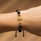 Mano de modelo usando una pulsera tejida en hilo de color negro con dije de cruz con esferas facetadas en oro amarillo de 18 quilates con bisutería de calidad de Joyería Caracas. 