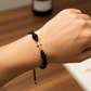 Mano de modelo usando una pulsera tejida en hilo de color negro con dije de cruz en oro amarillo de 18 quilates con bisutería de calidad de Joyería Caracas. 