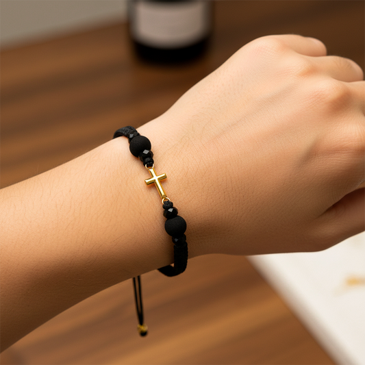 Mano de modelo usando una pulsera tejida en hilo de color negro con dije de cruz en oro amarillo de 18 quilates con bisutería de calidad de Joyería Caracas. 