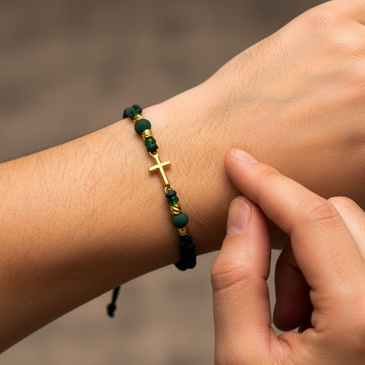 Mano de mujer usando una pulsera tejida de hilo color verde con bisutería de calidad de color verde, esferas facetadas y dije con forma de cruz en oro amarillo de 18 quilates de Joyería Caracas. 