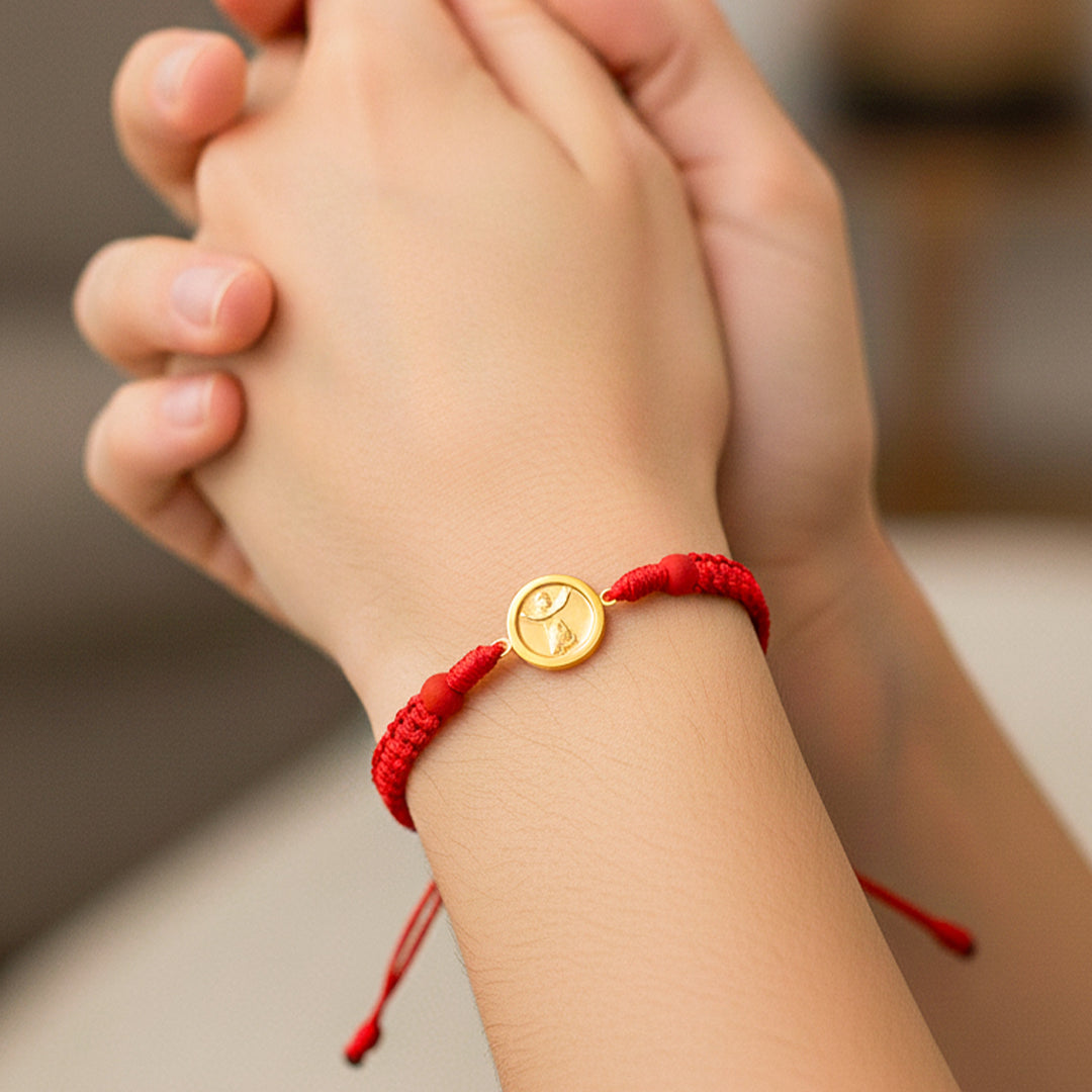 Mano de modelo usando una pulsera tejida en hilo color rojo con herraje del Divino Niño en oro amarillo de 18 quilates de Joyería Caracas. 