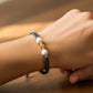 Mano de modelo usando una pulsera tejida en hilo color gris, esfera facetada en oro amarillo de 18 quilates con bisutería de calidad de Joyería Caracas. 