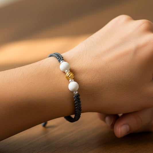 Mano de modelo usando una pulsera tejida en hilo color gris, esfera facetada en oro amarillo de 18 quilates con bisutería de calidad de Joyería Caracas. 