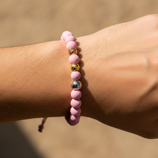 Mano de modelo usando una pulsera tejida en hilo de color rosa con esferas facetadas 3 oros de 18 quilates con bisutería de calidad de Joyería Caracas. 