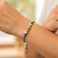 Mano de modelo usando una pulsera tejida en hilo color azul, esfera facetada y bisutería de calidad de Joyería Caracas. 