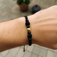 Mano de modelo usando una pulsera tejida en hilo color negro, con esfera facetada en oro amarillo de 18 quilates con bisutería de calidad de Joyería Caracas. 