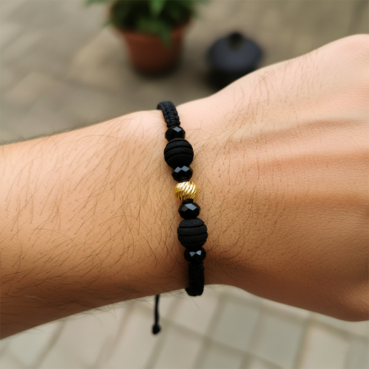 Mano de modelo usando una pulsera tejida en hilo color negro, con esfera facetada en oro amarillo de 18 quilates con bisutería de calidad de Joyería Caracas. 