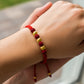Mano de mujer usando una pulsera tejida en hilo de color rojo, bisutería del mismo color y 3 esferas facetadas en oro amarillo de 18 quilates de Joyería Caracas. 