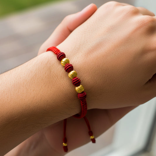 Mano de mujer usando una pulsera tejida en hilo de color rojo, bisutería del mismo color y 3 esferas facetadas en oro amarillo de 18 quilates de Joyería Caracas. 