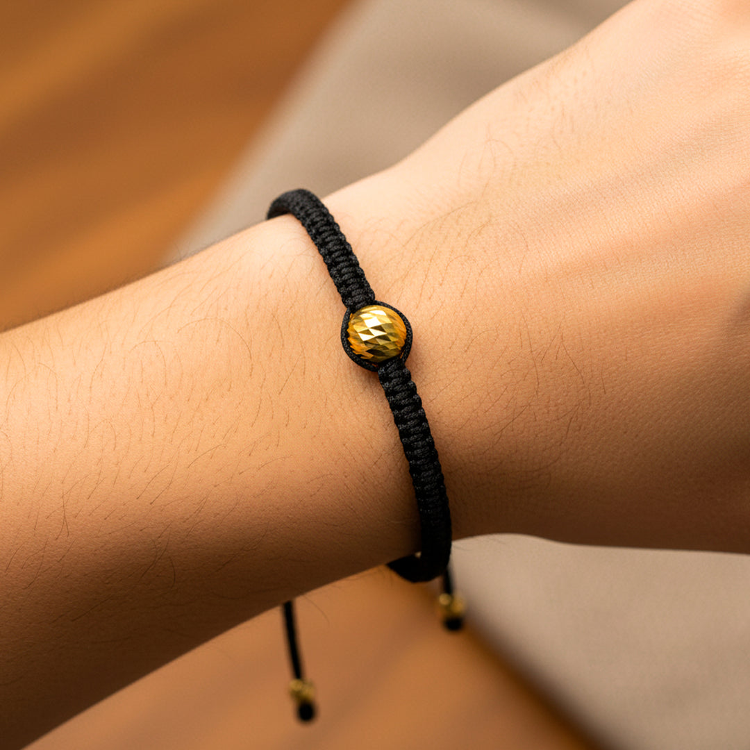 Mano de modelo usando una pulsera tejida en hilo color negro con esfera facetada en oro amarillo de 18 quilates de Joyería Caracas. 
