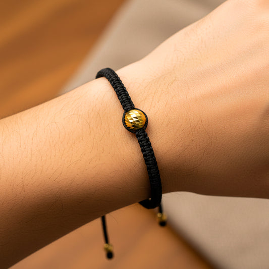 Mano de modelo usando una pulsera tejida en hilo color negro con esfera facetada en oro amarillo de 18 quilates de Joyería Caracas. 