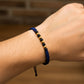 Mano de modelo usando una pulsera tejida en hilo color azul oscuro con esferas lisas en oro amarillo de 18 quilates de Joyería Caracas. 