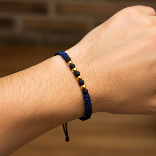 Mano de modelo usando una pulsera tejida en hilo color azul oscuro con esferas lisas en oro amarillo de 18 quilates de Joyería Caracas. 