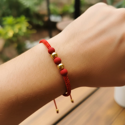Mano de modelo usando una pulsera tejida en hilo color rojo con 2 esferas lisas en oro amarillo de 18 quilates con bisutería de calidad de Joyería Caracas. 