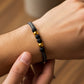 Mano de hombre usando una pulsera tejida en hilo combinado de color gris claro y oscuro con bisutería de color negro con 2 esferas lisas en oro amarillo de 18 quilates de Joyería Caracas. 